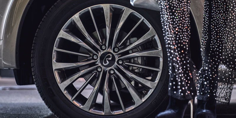 Close-up of Infiniti alloy wheel with a person standing nearby.